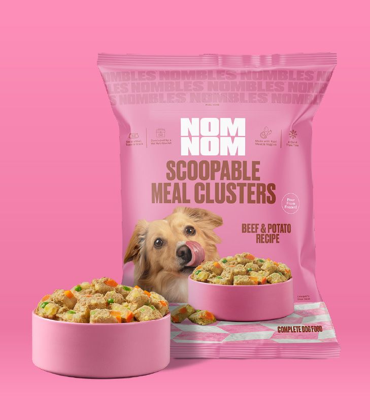 Nom Nom Scoopable Meal Clusters in pink packaging feature the Beef & Potato Recipe, 
        with a golden-colored dog pictured licking its nose. The bag highlights that the clusters 
        are complete dog food and can be poured from frozen for easy serving. Two pink bowls in 
        front show scoopable, bite-sized clusters with visible mix-ins, including orange and green 
        vegetable pieces, on a clean pink background.